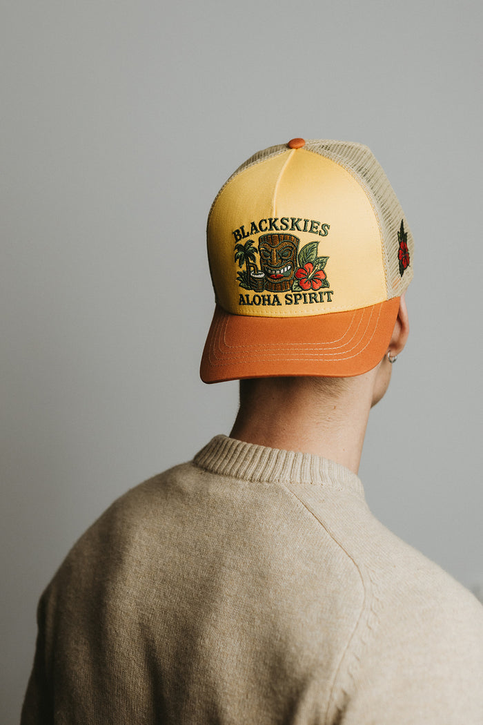 Person wearing a yellow and orange cap with 'Blackskies Aloha Spirit' branding on a gray background