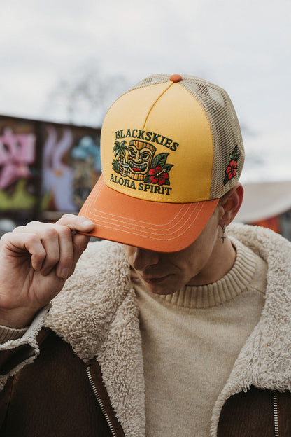 Person wearing a yellow and orange cap with 'Blackskies Aloha Spirit' design.