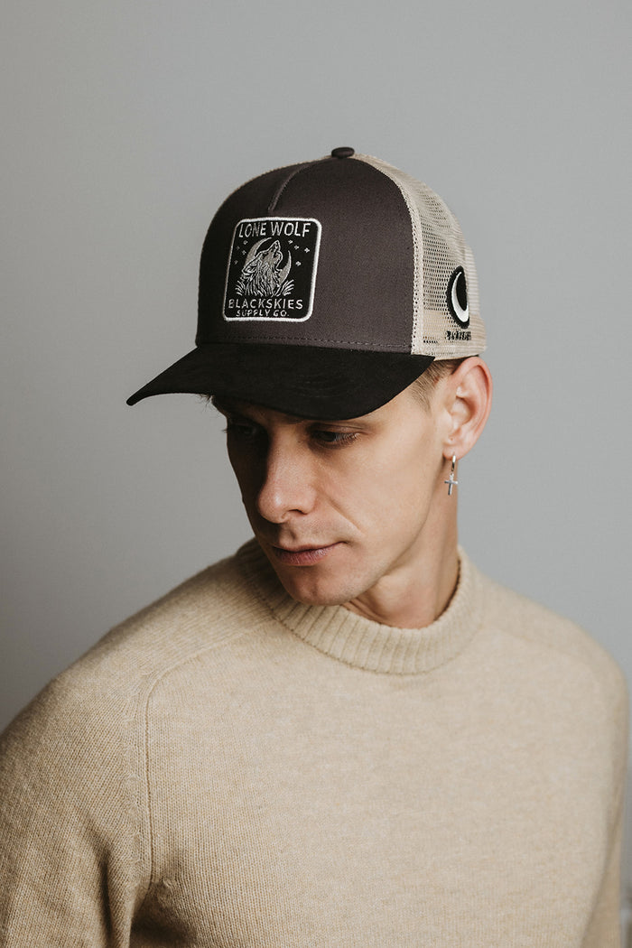Man wearing a black and beige cap with a logo on a gray background